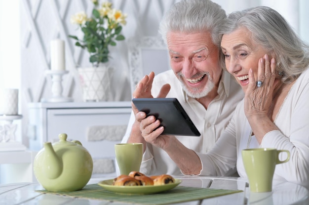 Happy senior couple using tablet while drinking tea at kitchen