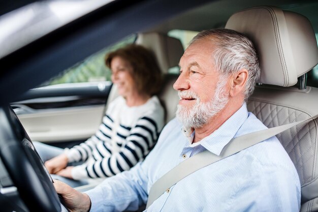 Happy senior couple with smartphone sitting in car driving