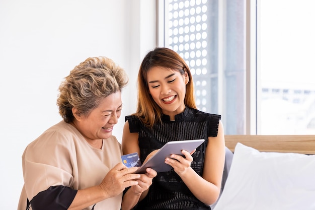 Happy senior elderly Asian woman female mother and daughter enjoy online shopping using digital tablet