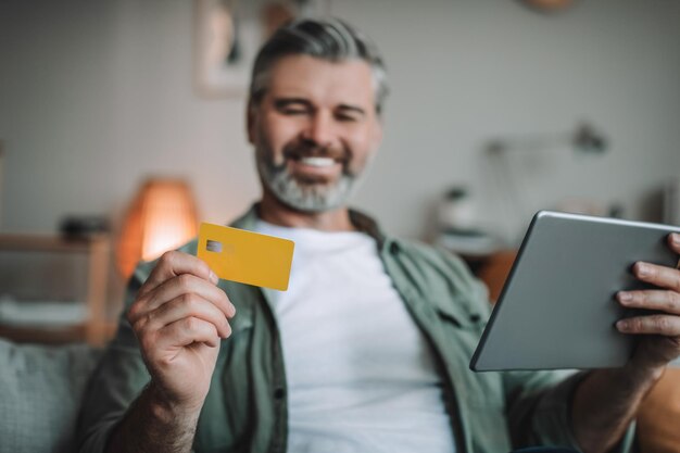 Happy senior european man with beard shopping online holding tablet and credit card enjoy huge sale