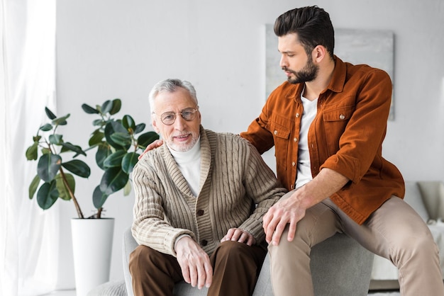 happy senior father in glasses sitting near handsome son at home