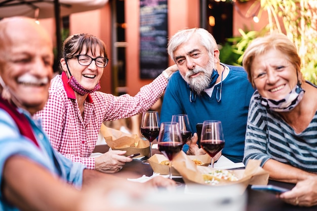 Happy senior friends taking selfie at restaurant with open face mask