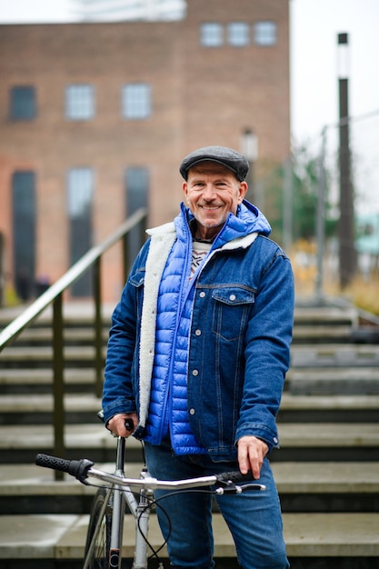 カメラを見て、街の屋外で自転車で通勤する幸せな年配の男性。