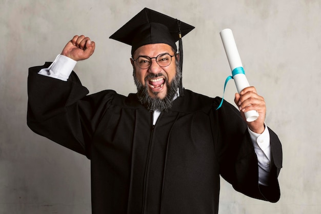 Uomo anziano felice in un abito di laurea che tiene il suo master