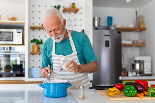 Happy senior man having fun cooking at home Elderly person preparing health lunch in modern kitchen Retired lifestyle time and food nutrition concept