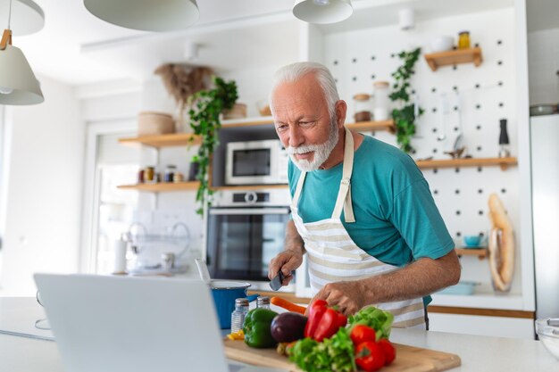 Happy senior man having fun cooking at home Elderly person preparing health lunch in modern kitchen Retired lifestyle time and food nutrition concept