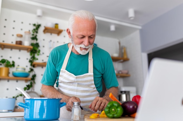 Happy senior man having fun cooking at home Elderly person preparing health lunch in modern kitchen Retired lifestyle time and food nutrition concept