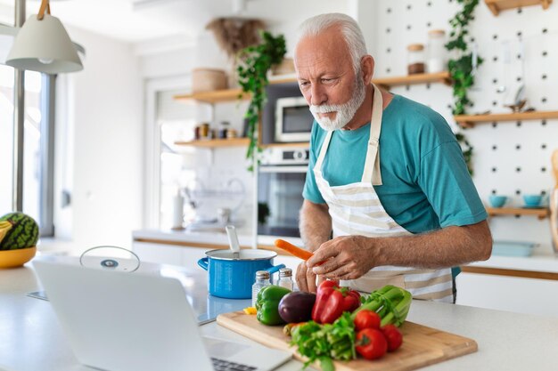 Happy senior man having fun cooking at home Elderly person preparing health lunch in modern kitchen Retired lifestyle time and food nutrition concept