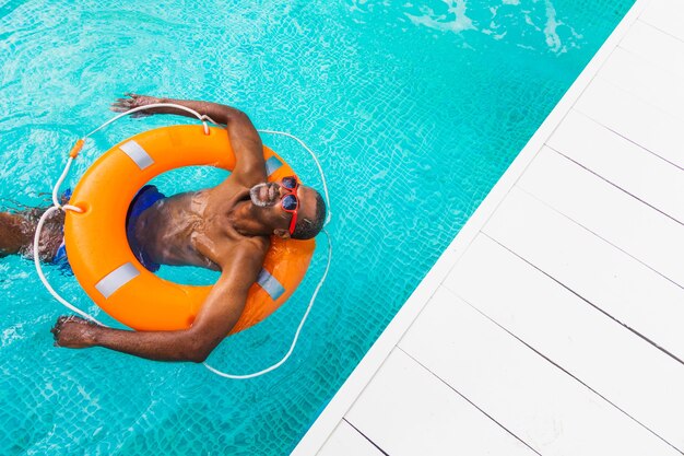 スイミングプールでパーティーをしている幸せな年配の男性-夏の間プライベートプールで日光浴とリラックスのアクティブな年配の男性