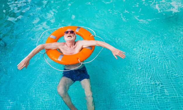 スイミングプールでパーティーをしている幸せな年配の男性-夏の間プライベートプールで日光浴とリラックスのアクティブな年配の男性