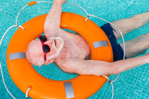 수영장에서 파티를 하는 행복한 노인 - 여름철에 개인 수영장에서 일광욕을 하고 휴식을 취하는 활동적인 노인 남성