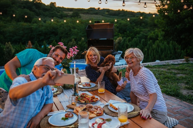 Photo happy senior man and his extended family taking selfie during dinner in the backyard