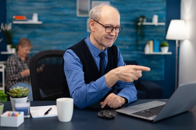 Happy senior man pointing at laptop during video conference