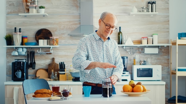 朝食のコーヒーを準備しながらフレンチプレスを押す幸せな年配の男性。ヴィンテージマグカップからの新鮮な茶色のカフェエスプレッソカップカフェインを楽しんでいる朝の高齢者、フィルターリラックスリフレッシュ