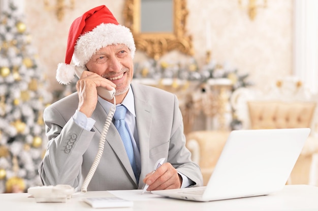 Happy senior man in Santa hat working with laptop at home