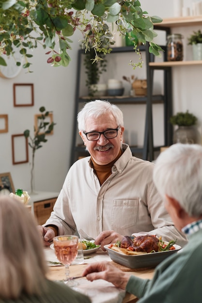 happy senior man sitting at the table and having dinner together with his friends at home