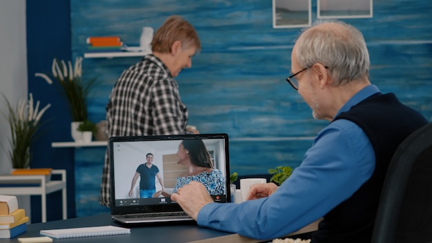 Uomo anziano felice che saluta durante la videoconferenza con i nipoti che usano il computer portatile in soggiorno. persona anziana che utilizza la webcam video con tecnologia di chat online su internet che effettua videochiamate per riunioni virtuali