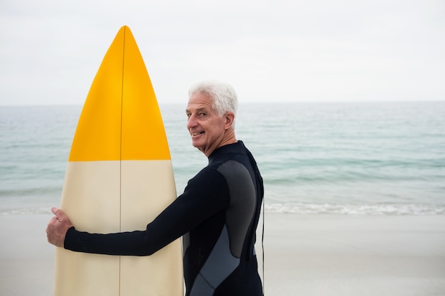 Happy senior man in wetsuit holding a surfboard