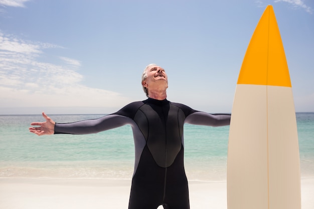 Happy senior man in wetsuit standing with arms outstretched 