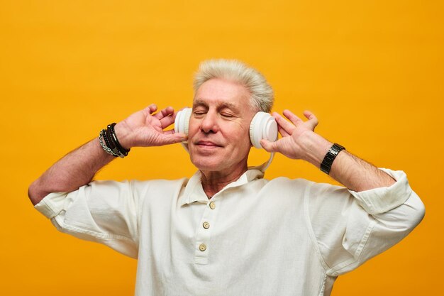 Happy senior man in white shirt touching headphones while enjoying music