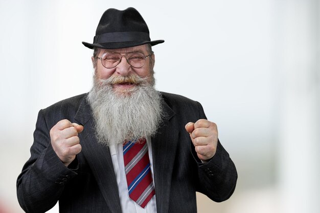 Happy senior man with clenched fists standing on blurred background.