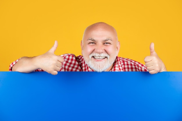Happy senior man with copy space on blank banner presenting product thumb up
