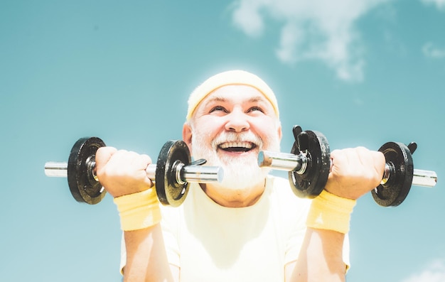 Happy senior man with dumbbell looking at camera senior male is enjoying sporty lifestyle senior man