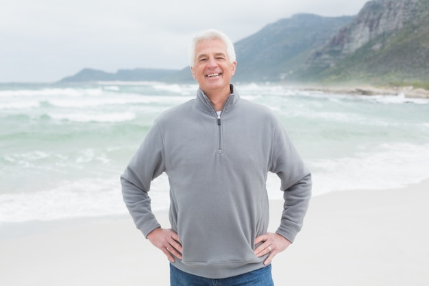 Happy senior man with hands on hips at beach