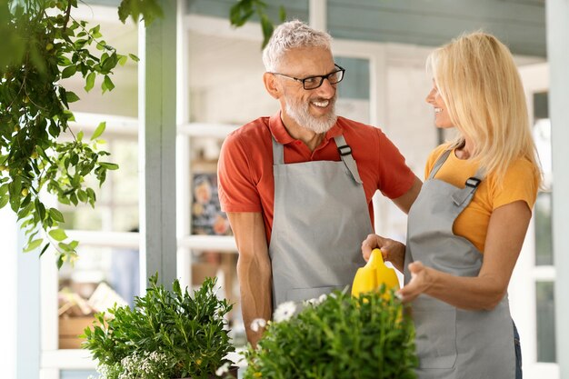 Happy senior man and woman in aprons watering flowers and chatting