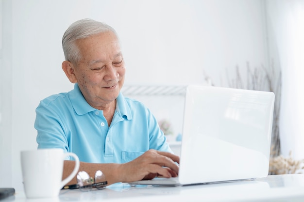 Happy senior man working on laptop and holding coffee cup at his home.