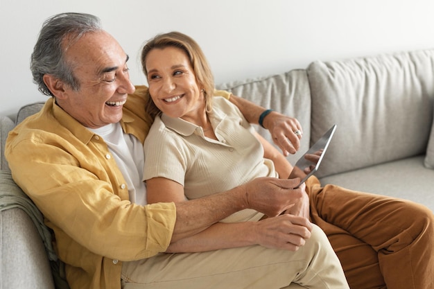 Happy senior married couple enjoying digital gadget world using tablet computer websurfing or watching film online