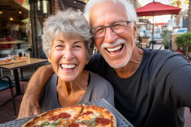 写真 幸せな年配の夫婦は伝統的なイタリアのピザ屋のレストランで外で一緒にピザを食べて楽しんでいます 座って話し合い笑っています 食べ物と高齢者のライフスタイルを楽しんでいる人々 観光