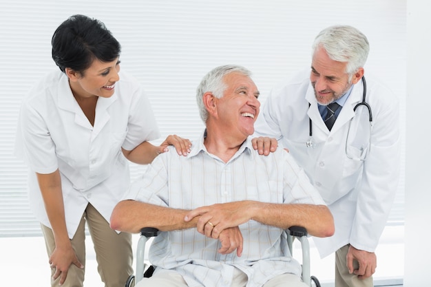 Счастливый старший пациента с врачами, сидя в инвалидной коляске