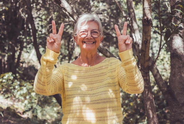 Happy senior smiling woman in the forest enjoying nature and freedom looking at camera gesturing