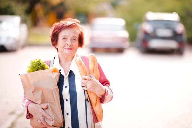 Photo happy senior woma holding package of food walking on street