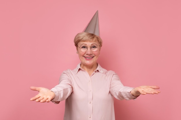 Happy senior woman celebrating and enjoying holiday or birthday party on pink background