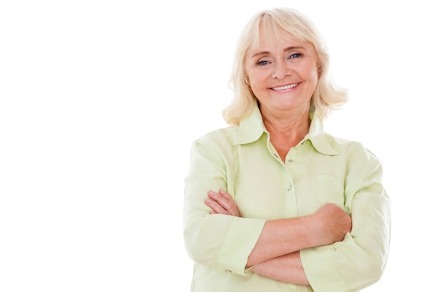 Happy senior woman. Cheerful senior woman keeping arms crossed and smiling while standing isolated on white background