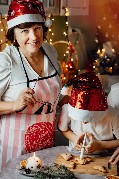 幸せな年配の女性は彼女の孫と一緒に家庭の台所でクリスマスのジンジャーブレッドを調理します垂直写真