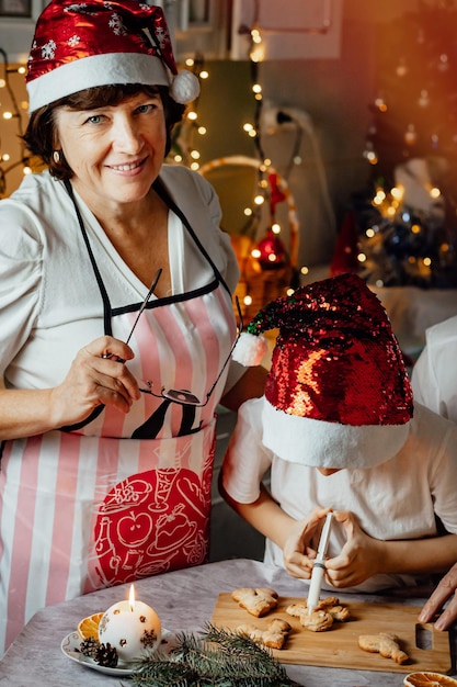 Una donna anziana felice cucina il pan di zenzero di natale nella cucina di casa con suo nipote foto verticale