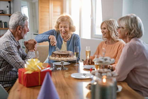 家で友達と誕生日を祝いながらケーキを切る幸せな年配の女性