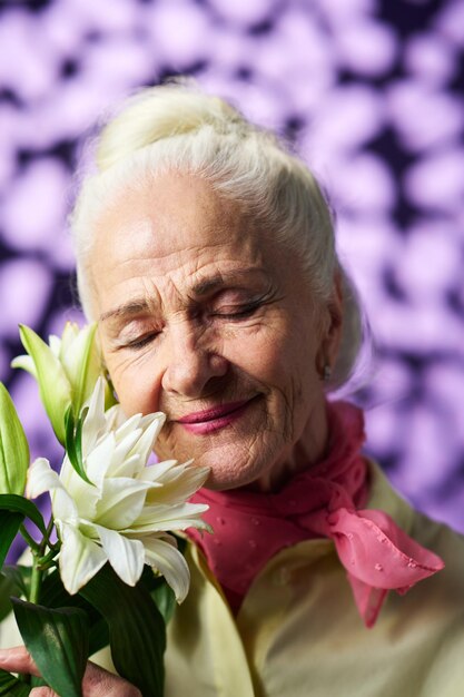 Happy senior woman enjoying nice smell of gorgeous white lily