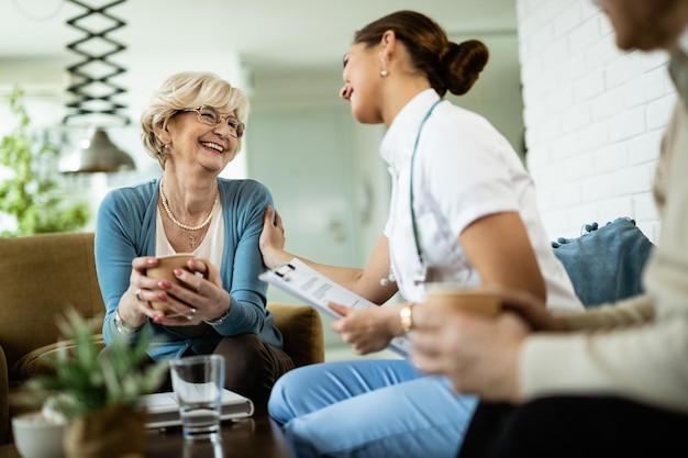 happy senior woman and female nurse talking during home visit