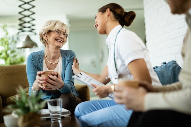 Happy senior woman and female nurse talking during home visit