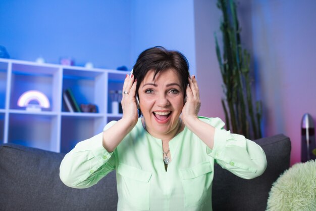 Happy senior woman in headphones listening to music at home. technology, people and lifestyle concept. positive pensioner meloman singing to music. active modern life after retirement