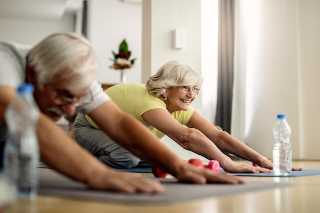 Foto felice donna senior e suo marito che si allungano sul pavimento mentre si esercita a casa