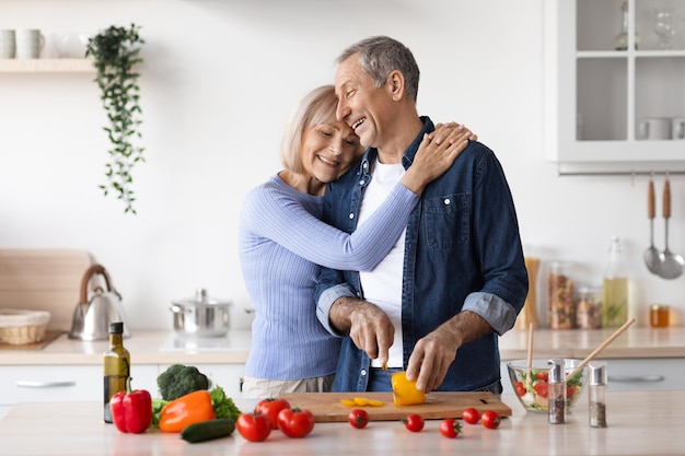 Happy senior woman hugging her husband cooking dinner