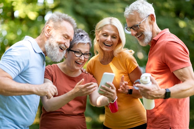 Счастливая старшая женщина показывает экран смартфона своим друзьям на открытом воздухе