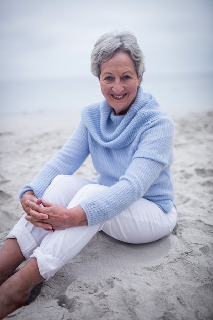 Donna senior felice che si siede sulla spiaggia