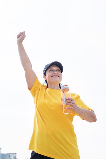 Happy senior woman in sports clothes exercising in the park standing with arms up