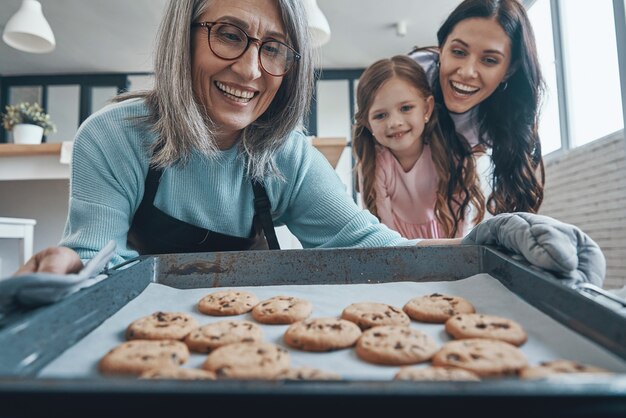 Foto felice donna anziana che tira fuori i biscotti dal forno e sorride mentre trascorre del tempo con la famiglia